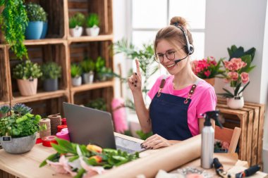 Çiçekçide çalışan sarışın, beyaz bir kadın video çekiyor. Bir fikir veya soruyla gülümsüyor. Mutlu yüzle işaret ediyor. 