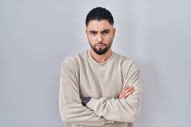 Soyutlanmış arka planda duran genç yakışıklı adam şüpheci ve gergin, yüzünde çapraz kollu tasvip etmeyen ifade. Negatif kişi. 