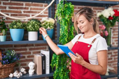 Young blonde woman florist smiling confident using touchpad at florist