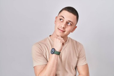 Young man standing over isolated background with hand on chin thinking about question, pensive expression. smiling with thoughtful face. doubt concept. 