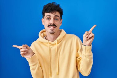Mavi arka planda duran İspanyol adam parmaklarıyla farklı yönleri işaret ederek gülümsüyor. reklam için kopyalama alanı 