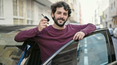 Young hispanic man smiling confident holding key of new car at street