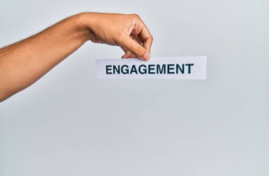 Beyaz arka planda nişan sözcüğü yazılı kağıt tutan beyaz bir adam.