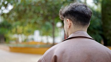 Genç Arap adam parkta geriye doğru duruyor.