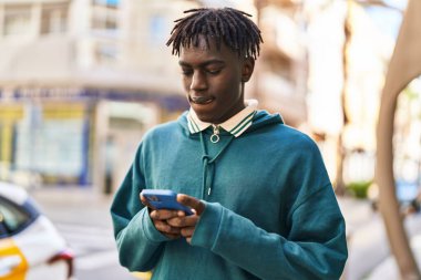 Afro-Amerikalı adam akıllı telefon kullanıyor ve sokakta ciddi bir ifade kullanıyor.