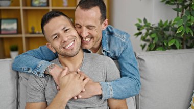 Two men couple hugging each other sitting on sofa at home