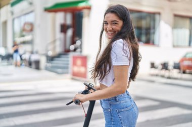 Young hispanic woman smiling confident using e-scooter at street