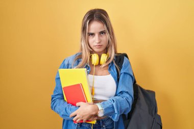 Sırt çantası takan, elinde kitap tutan, uykulu ve yorgun görünen, yorgunluktan bitkin ve akşamdan kalma, tembel gözlü genç sarışın bir kadın.. 