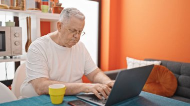 Middle age grey-haired man using laptop with relaxed expression at dinning room