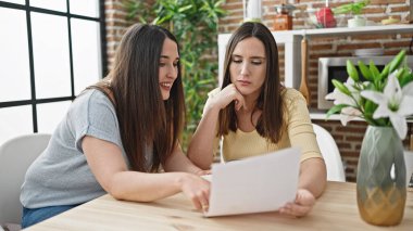 İki kadın yemek odasında masa başında oturmuş gazete okuyor.