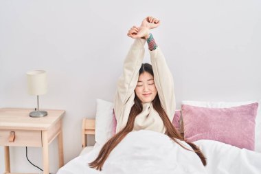 Chinese woman waking up stretching arms at bedroom