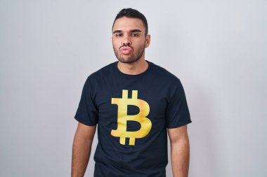 Bitcoin t-shirt giyen genç İspanyol adam kameraya bakıyor ve canlı yayında öpüşüyor. Güzel ve seksi. aşk ifadesi. 