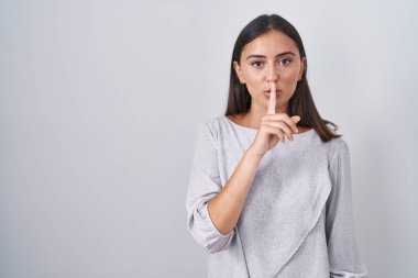 Young hispanic woman standing over white background asking to be quiet with finger on lips. silence and secret concept. 