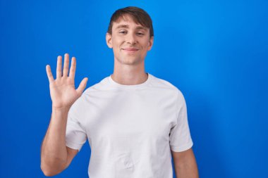 Beyaz, sarışın bir adam mavi arka planda duruyor. Mutlu ve gülümseyen bir merhaba diyor. Hoş geldin jesti. 