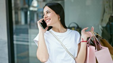 Genç, güzel İspanyol bir kadın elbise mağazasında akıllı telefondan konuşuyor.