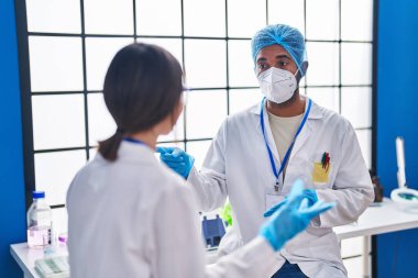 Erkek ve kadın bilim adamları gülümseyerek laboratuvarda kendinden emin konuşuyorlar.