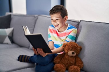 Genç, beyaz bir çocuk kanepede oturmuş kitap okuyor ve kahkahalarla gülüyor.. 