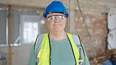 İnşaat alanında kendine gülen, orta yaşlı, gri saçlı bir inşaatçı.