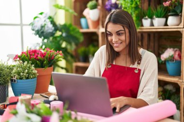 Young beautiful hispanic woman florist smiling confident using laptop at flower shop