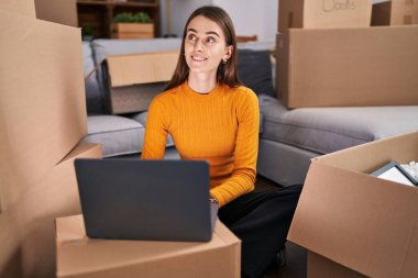 Young caucasian woman using laptop sitting on floor at new home