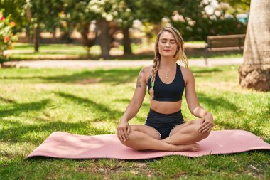 Park 'ta yoga eğitimi alırken gülümseyen genç bir kadın.