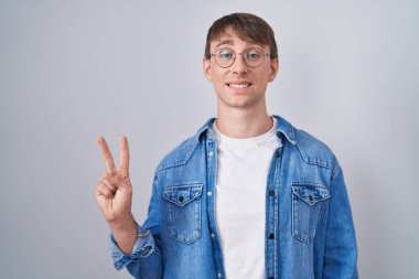 Beyaz, sarışın, gözlüklü, kendini beğenmiş ve mutlu bir şekilde gülümseyen iki numarayı işaret eden adam.. 