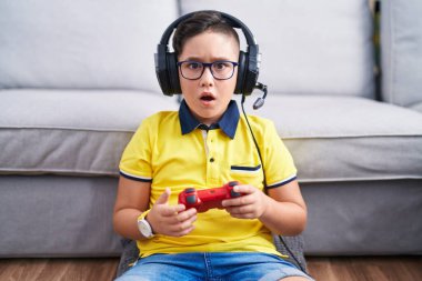 Şok olmuş kulaklık takmış video oyunu oynayan genç İspanyol çocuk şüpheci ve alaycı görünüyor, ağzı açık kalınca şaşırıyor. 