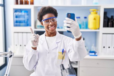 Afrika kökenli Amerikalı bir kadın bilim adamının laboratuarında çalışıyor. Akıllı telefonuyla video görüşmesi yapıyor. Gülümsüyor. 