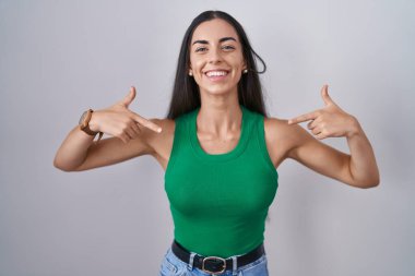 İzole edilmiş arka planda duran genç bir kadın. Yüzünde bir gülümseme, kendini gururlu ve mutlu olarak gösteren bir gülümseme.. 