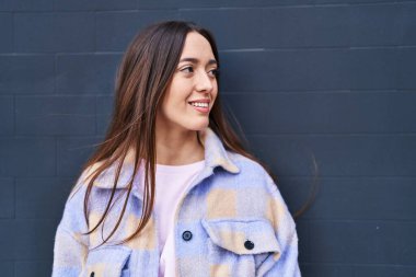 Genç, güzel İspanyol bir kadın, kendinden emin gülümsüyor ve izole edilmiş siyah bir arkaplanda yan tarafa bakıyor.