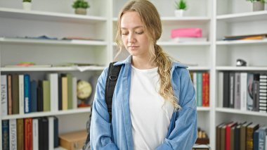 Kütüphanede sırt çantası takan genç, sarışın bir kız öğrenci.