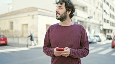 Genç İspanyol adam sokakta gülümseyen akıllı telefon kullanıyor.