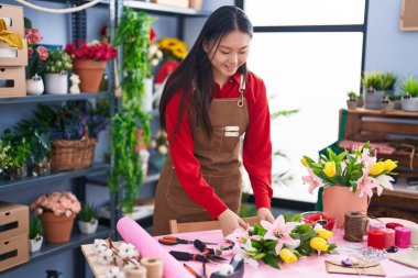 Genç Çinli kadın çiçekçi çiçekçide çiçek buketi yapıyor.