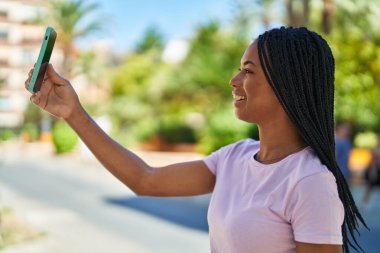 Afro-Amerikalı kadın, parkta akıllı telefonun yanında kendinden emin bir şekilde selfie çekiyor.