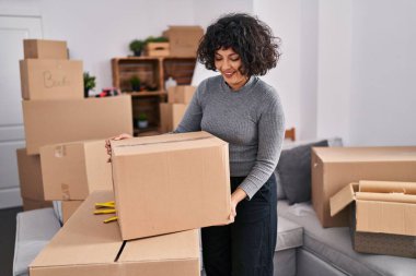 Young beautiful hispanic woman smiling confident holding package at new home
