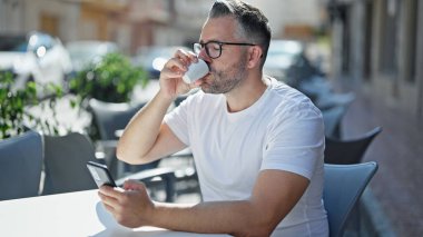 Kahve dükkanının terasında kahve içen gri saçlı adam.