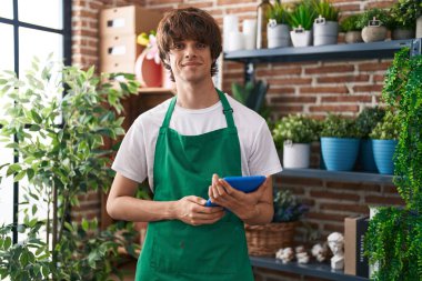 Young blond man florist smiling confident using touchpad at flower shop