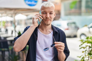 Genç beyaz adam gülümsüyor. Kendine güveniyor. Akıllı telefondan konuşuyor.