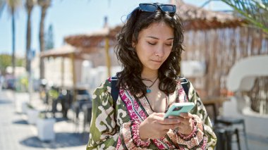 Kahve dükkanının terasında akıllı telefon kullanan genç ve güzel bir İspanyol kadın.