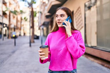 Young woman talking on the smartphone drinking coffee at street