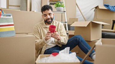 Young hispanic man unpacking cardboard box at new home