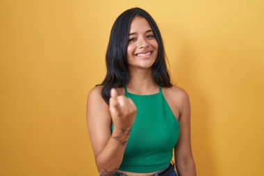 Sarı arka planda duran esmer kadın seni çağırıyor. El kol hareketi yap. Mutlu bir şekilde karşıla ve gülümse. 