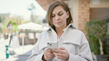 Orta yaşlı İspanyol kadın sokakta akıllı telefon kullanıyor.