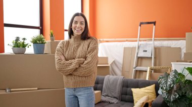 Young beautiful hispanic woman smiling confident standing with arms crossed gesture at new home