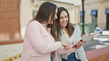 Sokakta akıllı telefon kullanan kendine güvenen iki kadın.