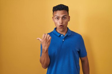 Sarı arka planda dikilen İspanyol genç adam elleri yana doğru işaret ederek şaşırdı, ağzı açık hayret içinde kaldı.. 