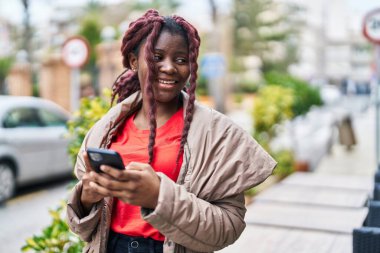 Afro-Amerikalı kadın sokakta akıllı telefon kullanarak kendine güveniyor.