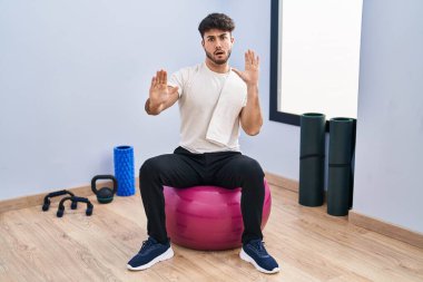 Sakallı İspanyol bir adam yoga odasında pilatese oturmuş korkmuş ve korkudan dehşete düşmüş halde. El hareketlerini durdur, şok içinde bağır. panik konsepti. 