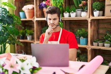 Çiçekçide çalışan Latin asıllı genç bir adam kameraya kollarını kavuşturup çenesine bakarak gülümsüyor. Olumlu düşünmek. 