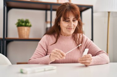 Antijen covid-19 testi yapan orta yaşlı bir kadın evdeki masada oturuyor.